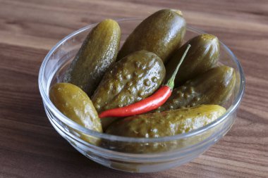 Ahşap zemin üzerinde kırmızı biber yığını olan yeşil salatalık turşusu, lezzetli atıştırmalık konsepti, vegan yemeği..