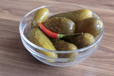 Ahşap zemin üzerinde kırmızı biber yığını olan yeşil salatalık turşusu, lezzetli atıştırmalık konsepti, vegan yemeği..