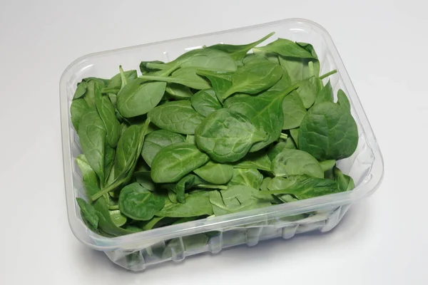 Beyaz arka planda plastik ambalajlı ıspanak satılmaya hazır, vegan yemeği. İş konsepti.