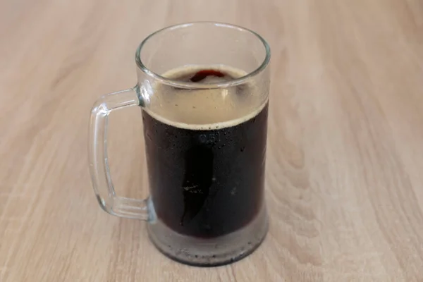 パブの木のテーブルの上に冷たい暗いビールの湿ったマグカップ — ストック写真