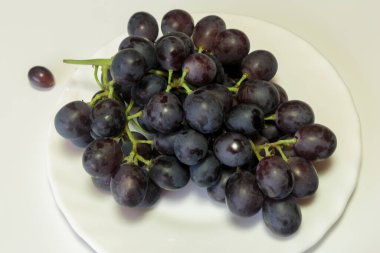 Beyaz tabakta kırmızı bir üzüm dalı. Vejetaryen yemeği.