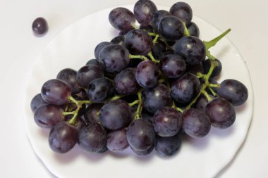 Beyaz tabakta kırmızı bir üzüm dalı. Vejetaryen yemeği.