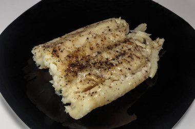 Siyah bir tabakta haşlanmış morina balığı. Beslenme yemeği. Lezzetli.