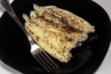 Siyah bir tabakta haşlanmış morina balığı. Beslenme yemeği. Lezzetli.