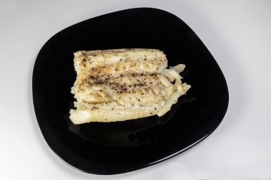 Siyah bir tabakta haşlanmış morina balığı. Beslenme yemeği. Lezzetli.