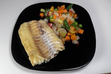 Siyah bir tabakta sebzeli haşlanmış morina balığı. Beslenme yemeği. Lezzetli.