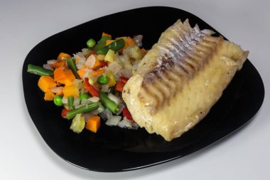 Siyah bir tabakta sebzeli haşlanmış morina balığı. Beslenme yemeği. Lezzetli.