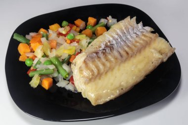 Siyah bir tabakta sebzeli haşlanmış morina balığı. Beslenme yemeği. Lezzetli.