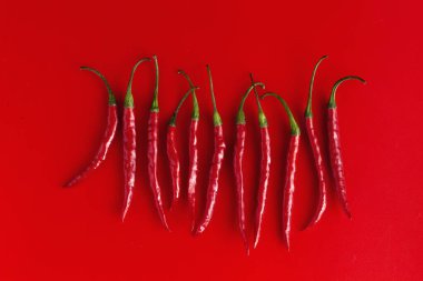 Kırmızı arka planda arka arkaya 11 kırmızı biber. Tepeden çekim