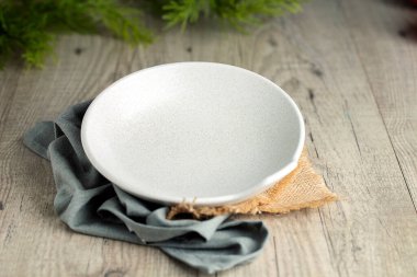 Mavi peçete ve çuval bezi üzerine beyaz bir tabak. Ahşap zemin ve yeşil bitkiler