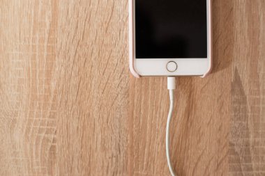 Beyaz telefon masanın üstünde ve şarj cihazına bağlı.