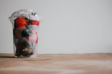 Kahverengi ahşap masada bir plastik şeffaf fincan çilek. Sağlıklı kahvaltı.