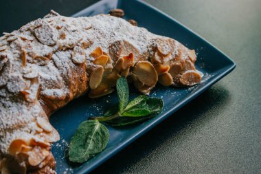 Koyu bir arka plan üzerinde tabakta pudra şekeri ve nane ile lezzetli kruvasan