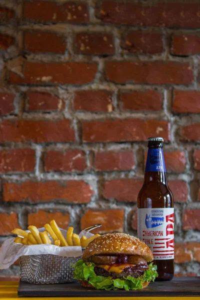 Hamburguesas caseras con pera de res y cereza y papas fritas y botella de cerveza fría sobre mesa de madera sobre un fondo de ladrillo — Foto de Stock