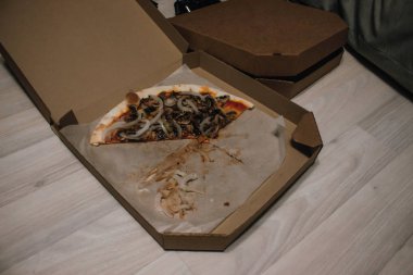 Parti veya öğle yemeğinden sonra pizza görünümü. Yiyecek israfı. Soğan, mantar, dilimlerde et. Yerde karton kutu.