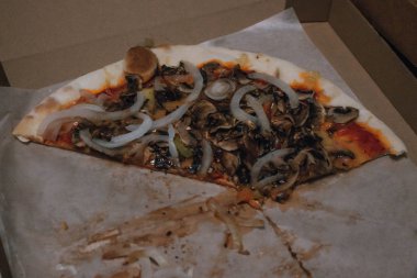 Parti veya öğle yemeğinden sonra pizza görünümü. Yiyecek israfı. Soğan, mantar, dilimlerde et. Yerde karton kutu.