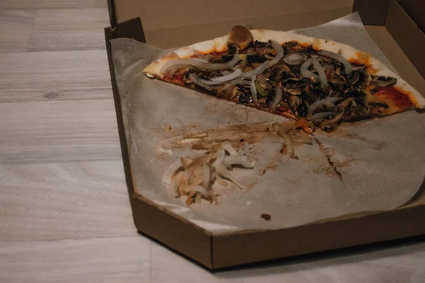 Pizza view after party or lunch. Food waste. Onion, mushrooms, meat on slices. Cardboard box on the floor. — Stock Photo, Image