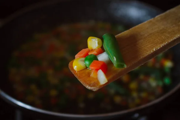 Fried vegetable mix on black skillet. Stewed sliced vegetables on a pan. Frozen vegan breakfast preparation. Using paddle.