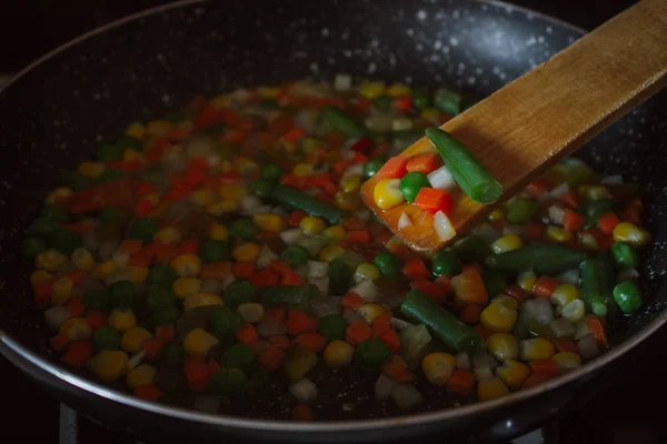 Fried vegetable mix on black skillet. Stewed sliced vegetables on a pan. Frozen vegan breakfast preparation. Using paddle.