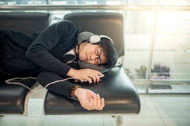 Genç Asyalı adam gözlük ve Uluslararası Havaalanı terminal, seyahat yaşam biçimi uçuş bağlanmak için beklerken kürsüde uyuma kulaklık
