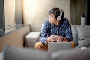 Genç Asyalı adam kulaklıklarla müzik, bir mola ve yaşam alanı, rahat kentsel yaşam tarzı kavramları rahatlatıcı için smartphone kullanarak