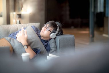 Kütüphane, yüksek okul veya üniversite üniversite öğrencisi, eğitim kavramı çalışma sırasında kanepede şekerleme sahip müzik, dinlemek için smartphone kullanan genç Asyalı adam