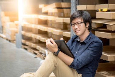 Genç Asyalı adam stocktaking ürünün depoda raf karton kutu, dijital tablet kullanarak yapıyor. fiziksel envanter sayım kavramı
