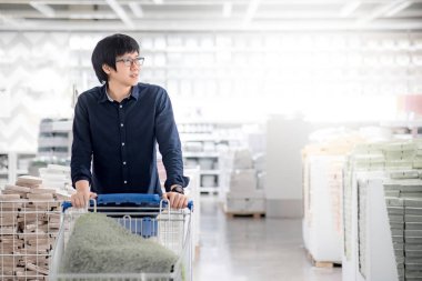 Ne satın almak tercih tramvay arabası kullanan genç Asya mutlu adam. Ev geliştirme malzeme ambarı toptan kavramı içinde alışveriş