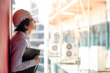 Genç Asyalı mühendis veya mimar inşaat alanında kişisel koruyucu ekipman kask giyen süre dosyaları tutan. Mühendislik, Mimarlık ve inşaat iş kavramları
