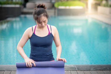 Genç Asyalı çekici kadın mor yoga mat Yüzme Havuzu, açık pilates egzersiz ve sağlıklı yaşam kavramları haddeleme