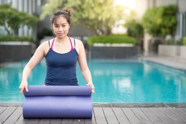 Genç Asyalı çekici kadın mor yoga mat Yüzme Havuzu, açık pilates egzersiz ve sağlıklı yaşam kavramları haddeleme