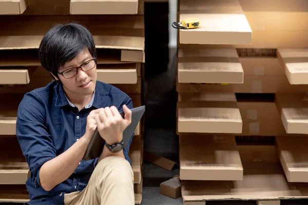 Genç Asyalı adam stocktaking ürünün depoda raf karton kutu, dijital tablet kullanarak yapıyor. fiziksel envanter sayım kavramı