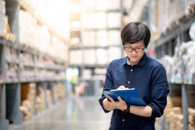 Genç Asyalı adam stocktaking ürünün depoda raf karton kutu, Pano ve kalem kullanarak yapıyor. fiziksel envanter sayım kavramı
