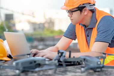 Genç Asyalı adam dron laptop ve smartphone inşaat alanında çalışma. İnsansız hava aracı (İHA) arazi için kullanarak ve inşaat mühendisliği proje sitesi anket oluşturma.