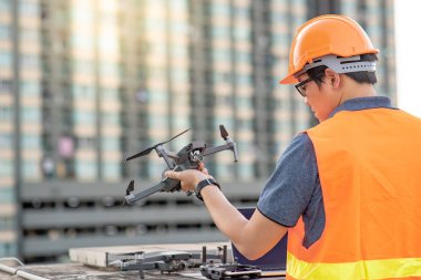 Genç Asyalı adam dron laptop ve smartphone inşaat alanında çalışma. İnsansız hava aracı (İHA) arazi için kullanarak ve inşaat mühendisliği proje sitesi anket oluşturma.