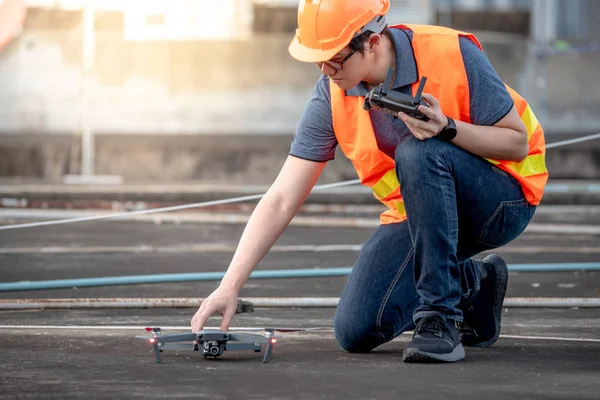Young Asian engineer using drone at construction site. Using unmanned aerial vehicle (UAV) for land and building site survey in civil engineering project.