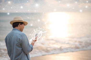 Genç Asyalı adam Smartphone ile parlayan mobil uygulama simgesi hologram tropik sahilde günbatımı sırasında kullanarak. Küresel iletişim ağı ve Internet şey (çok). Yaz tatil yaşam tarzı kavramları
