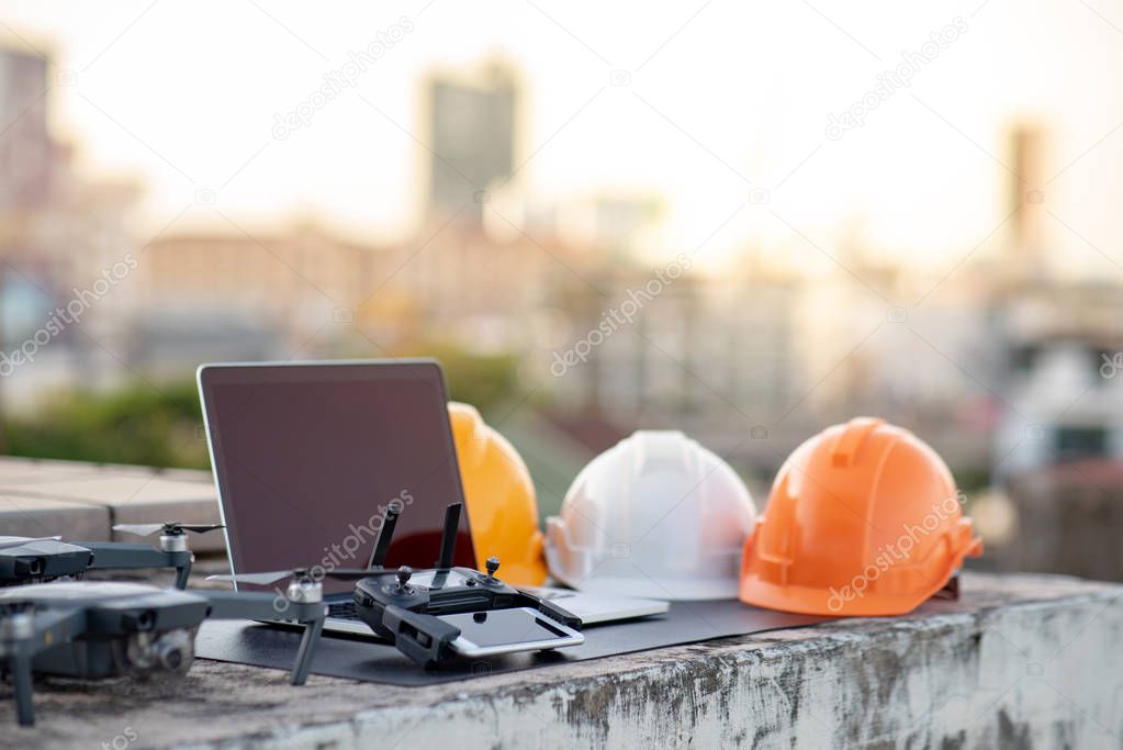 Drone, smartphone, laptop computer and protective helmet at construction site. Using unmanned aerial vehicle (UAV) for land and building site survey in civil engineering project.