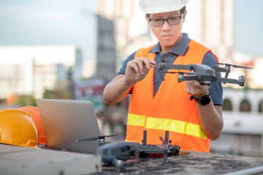 Genç Asyalı adam dron laptop ve smartphone inşaat alanında çalışma. İnsansız hava aracı (İHA) arazi için kullanarak ve inşaat mühendisliği proje sitesi anket oluşturma.