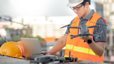 Küçük Asya mühendislik dron laptop ve smartphone ile inşaat alanında çalışan adam. İnsansız hava aracı (İHA) arazi için kullanarak ve inşaat mühendisliği proje sitesi anket oluşturma.