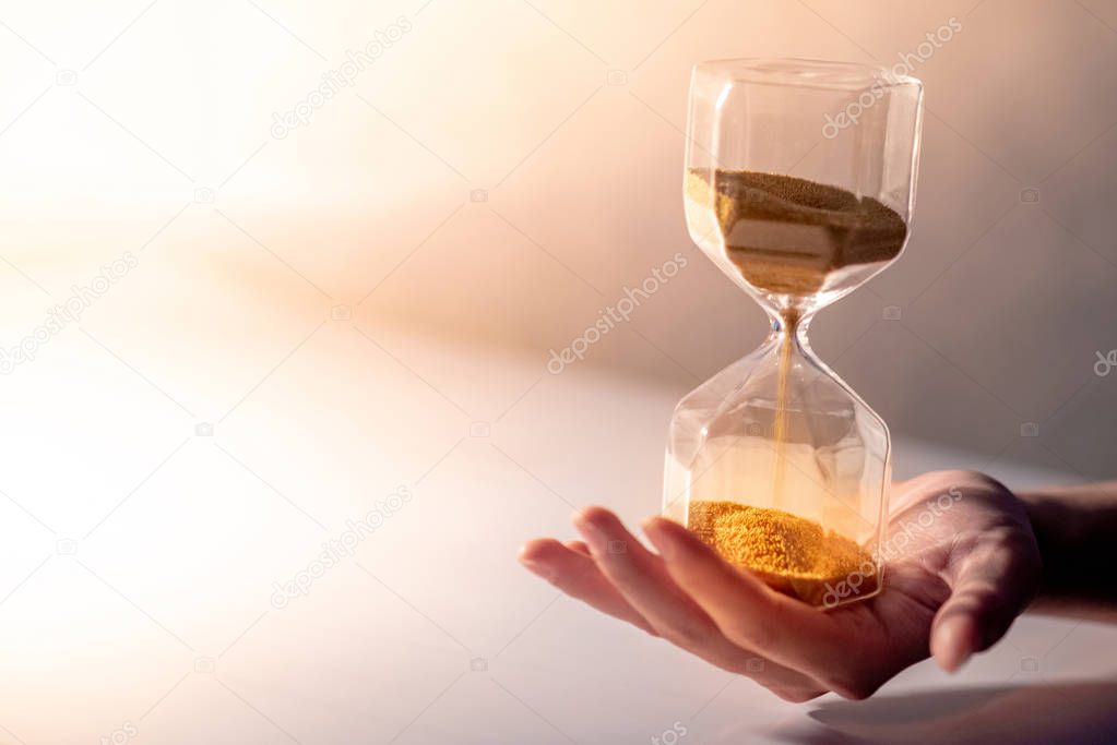 Close up of gold sand running through the shape of modern hourglass on male hand.Time passing and running out of time. Urgency countdown timer for business deadline concept with copy space