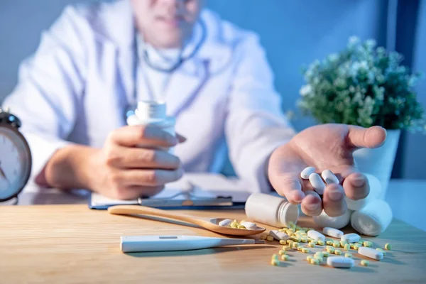 Male Asian doctor showing pills on his hand. Doctor working with medicine paperwork on the desk in clinic or hospital. Medical treatment and health care concepts.