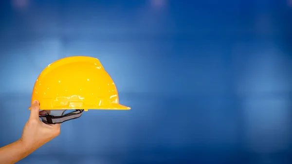 Male engineer hand holding personal yellow protective safety helmet on blue background. Architecture, Construction and Engineering concepts