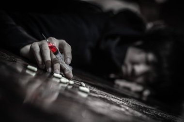 Keş adam uyuşturucu iğne şırınga ve hapları tutarak yerde yatıyor. Uyuşturucu aşırı doz ve bağımlılık kavramı ölümden