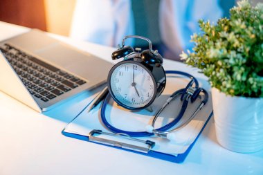Mavi stetoskop, pano, kalem, tablo Doktor Resepsiyon saat ve dizüstü bilgisayarda. Bulanık beyaz doktor ceket içinde belgili tanımlık geçmiş. Tıbbi tedavi ekipman ve sağlık tanı kavramları