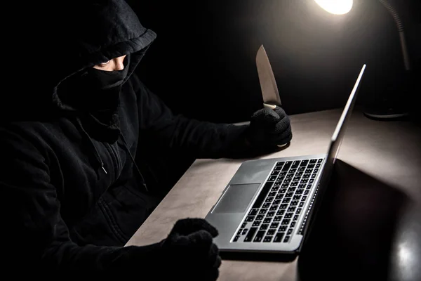 Male hacker threading laptop computer with knife. Cyber attack and internet data security concept