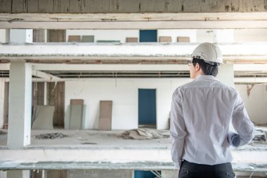 Asyalı erkek mühendis veya mimar planları veya inşaat alanında koruyucu güvenlik kask giyen süre mimari çizim tutmak. Mühendislik, Mimarlık ve inşaat kavramlar bina