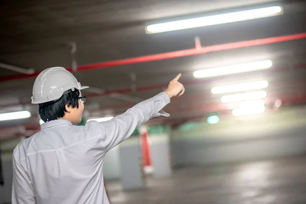 Young Asian male engineer or architect pointing wearing protective safety helmet on red stair at construction site. Civil engineering, Architecture and building construction concept