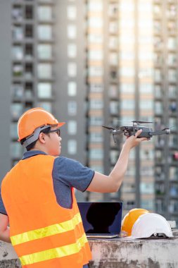 Küçük Asya mühendislik dron laptop ve smartphone ile inşaat alanında çalışan adam. İnsansız hava aracı (İHA) arazi için kullanarak ve inşaat mühendisliği proje sitesi anket oluşturma.