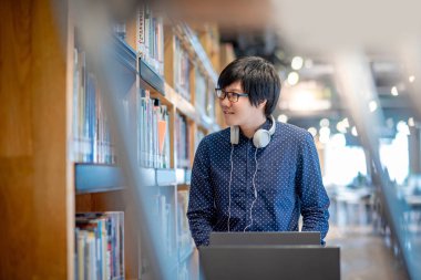 Genç Asyalı adam öğrenci kitap sepeti Halk Kütüphanesi, eğitim araştırma ve kendi Üniversitesi yaşam kavramları öğrenme içinde bookshelf kitap seçimi ile